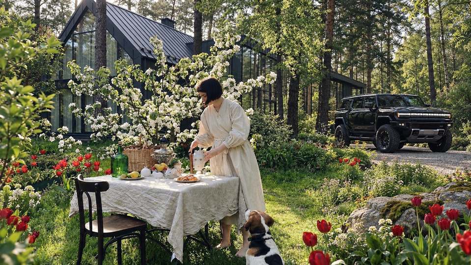 A woman sets an outdoor table beside a black HUMMER EV at a modern second home