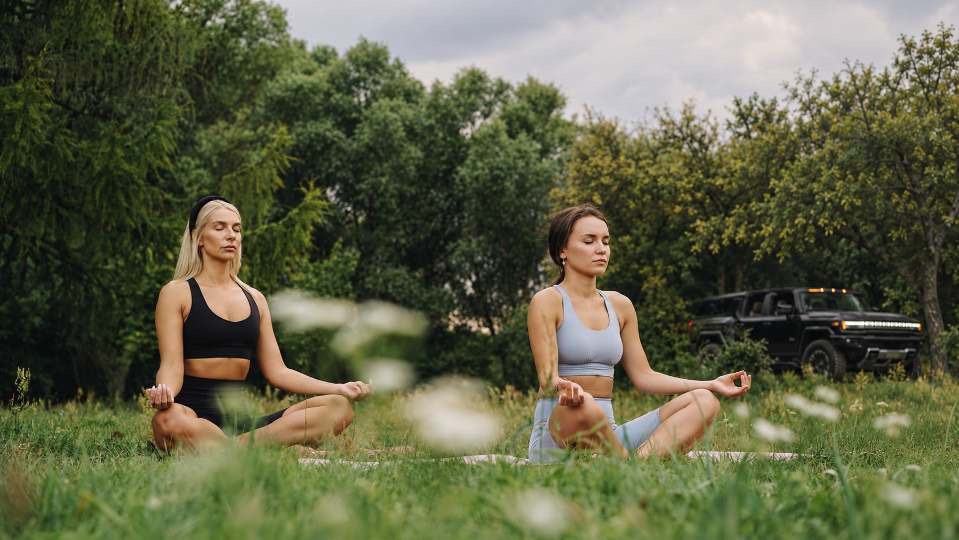 Two women practise yoga in a meadow with a HUMMER EV parked behind